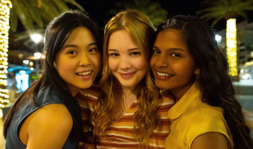 Three teenage girls standing closely in a line, smiling
