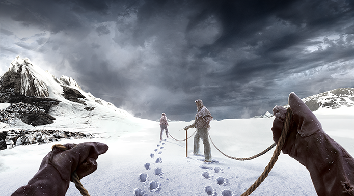 The frozen tundra, gloved hands hold a rope and two snowsuit clad people traverse ahead.