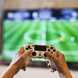 A pair of hands holding a video game controller in front of a TV screen