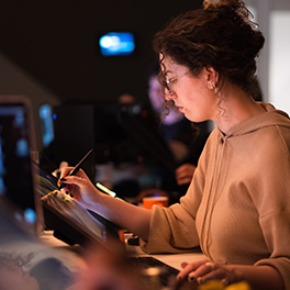 A woman sitting at a desk using a stylus pen to work on a device