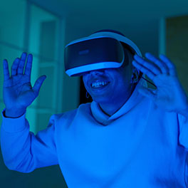 A man wearing a VR headset holding his hands up, bathed in blue light