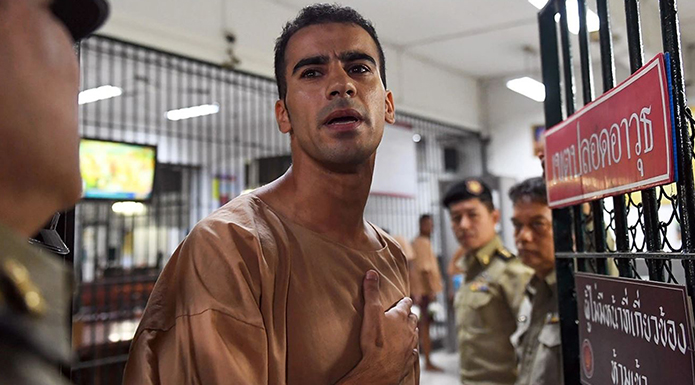 A man in a prison uniform being shown through a security gate by a guard