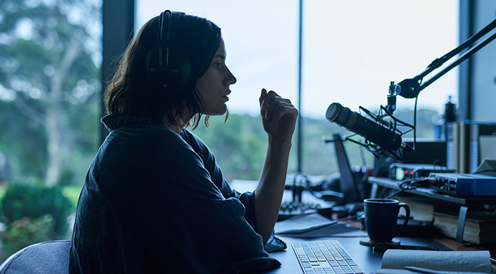 A young woman wearing headphones sits in front of a microphone