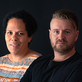 A photo of a woman in a colourful shirt next to a bearded man in a black shirt, on a black background