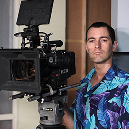 A man wearing a purple and blue shirt standing behind a camera