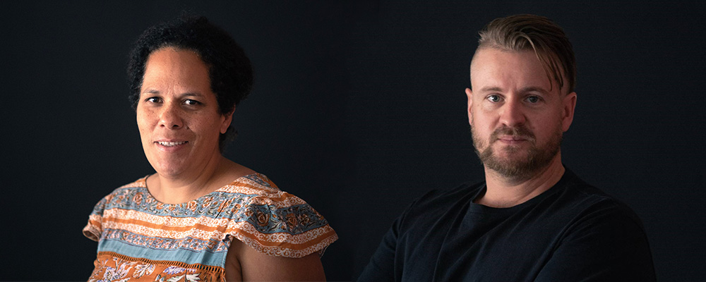 A photo of a woman in a colourful shirt next to a bearded man in a black shirt, on a black background