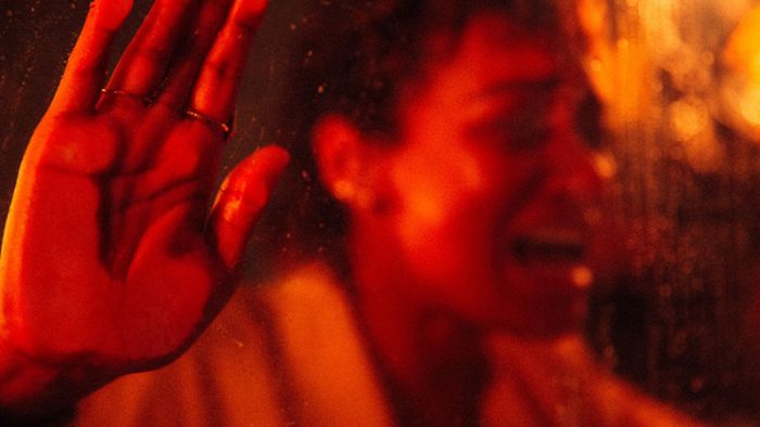 A photo of a woman behind a sheet of glass holding her hand to the glass and screaming