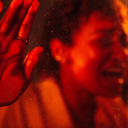 A photo of a woman behind a sheet of glass holding her hand to the glass and screaming