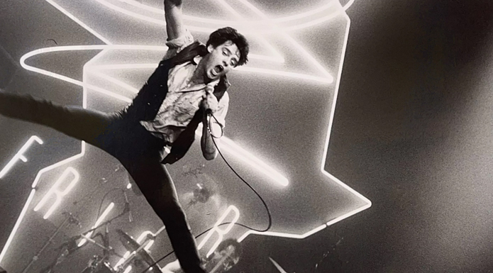 Black and white photo of a man on stage jumping holding a microphone and singing