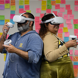 A man and a woman wearing VR headsets standing back to back