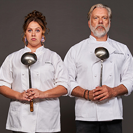 Natalie Abbott and Erik Thomson standing side by side wearing chef's whites and holding ladles