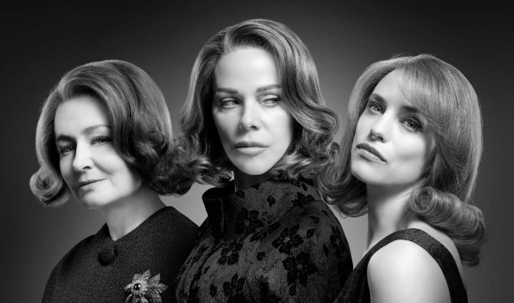 Actors Miranda Otto, Debi Mazar and Jessica De Gouw stand against a plain background in 60's style fashion and hair-dos. The image is in black and white.