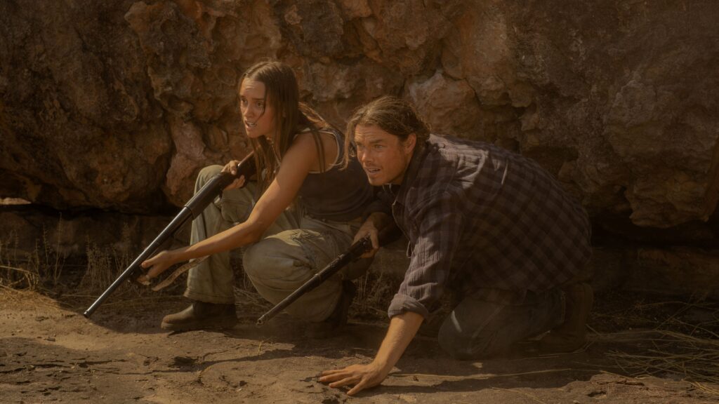 Territory_Netflix_12951 Kylah Day and Sam Corlett in Territory hold shotguns, crouched near the ground.