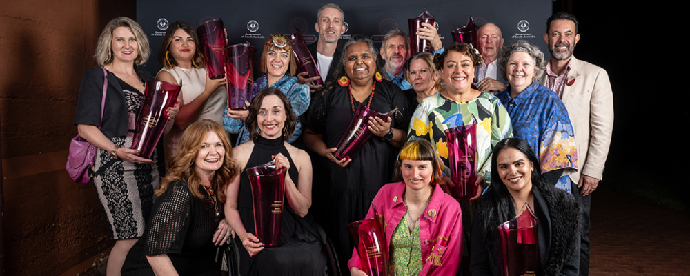 A group of people pose with large red glass awards.