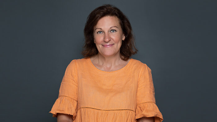 A woman in an orange shirt stands in front of a dark green background