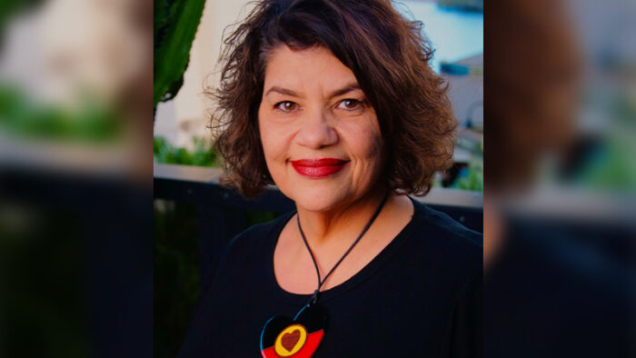 Kirstie Parker smiles at the camera. She's wearing a necklace with a heart-shaped pendant in the Aboriginal flag colours.