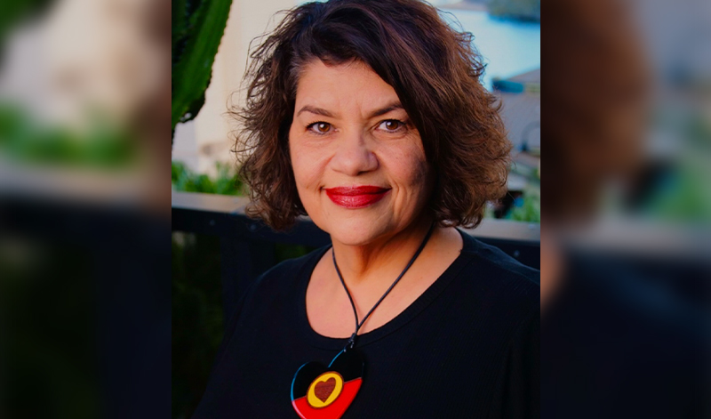 Kirstie Parker smiles at the camera. She's wearing a necklace with a heart-shaped pendant in the Aboriginal flag colours.