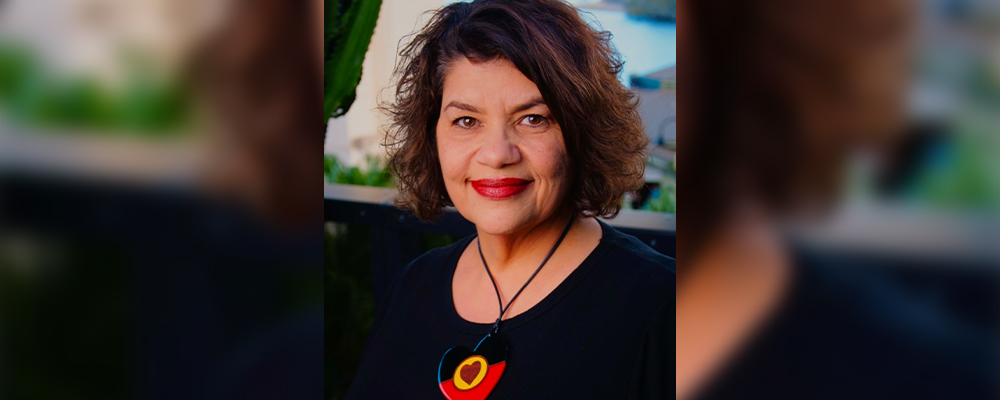 Kirstie Parker smiles at the camera. She's wearing a necklace with a heart-shaped pendant in the Aboriginal flag colours.