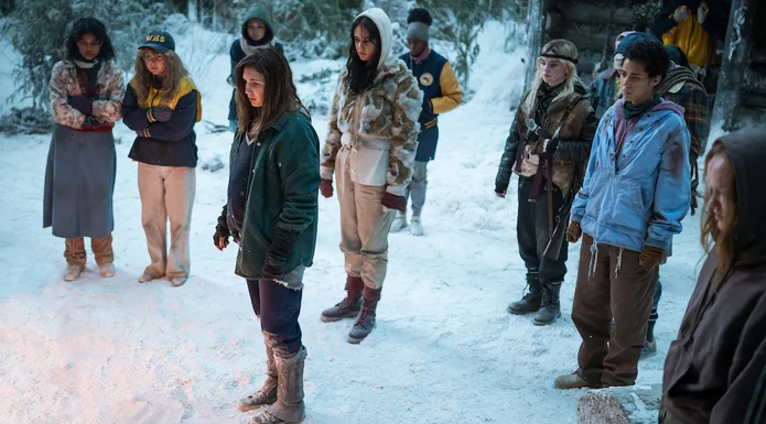 A group of young women stand around a snowy forest.