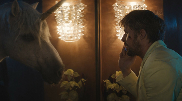 Ryan Gosling in the fall guy looks at a unicorn. There is a cut on his cheek.