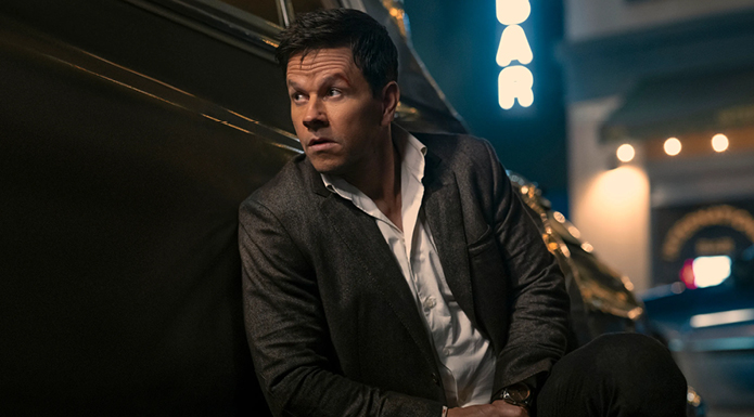 Mark Wahlberg in Play Dirty crouches behind a car.