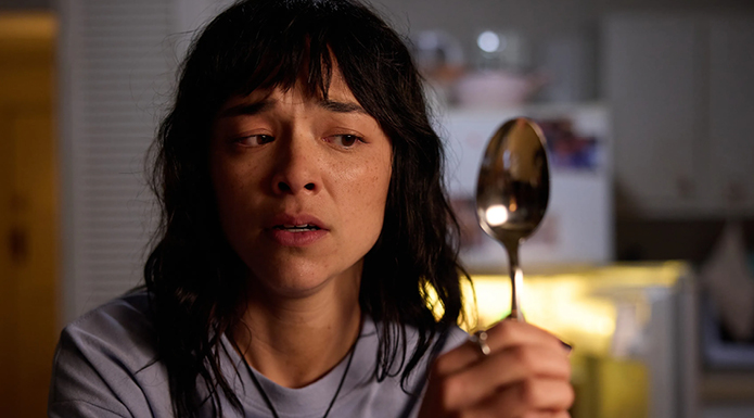 A frightened looking woman holds a spoon in front of her face.