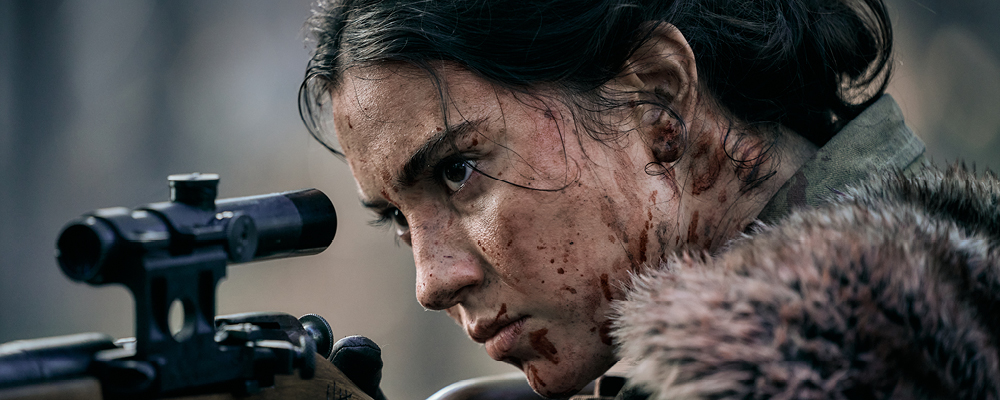 Lady Death A dark haired woman with blood splattered all over her face looks into the scope of a rifle.